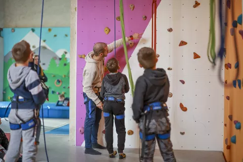 animateur face à un mur d'escalade et qui aide des enfants