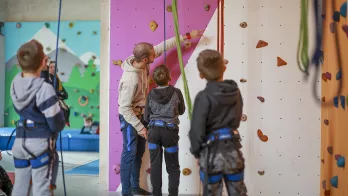 animateur face à un mur d'escalade et qui aide des enfants
